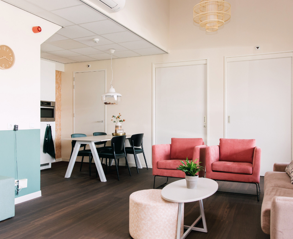 Zorginterieur met comfortabele zitplekken en eethoek voor een huiselijke woonzorgomgeving.